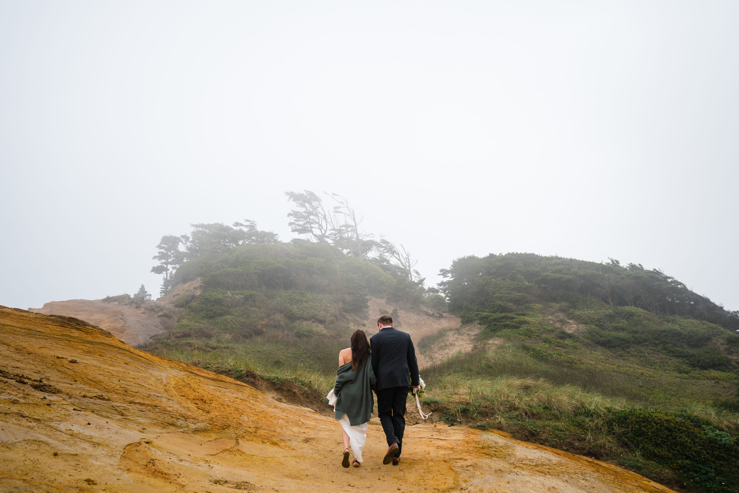 bride and groom walking up to cape kiwanda for their elopement on the oregon coast